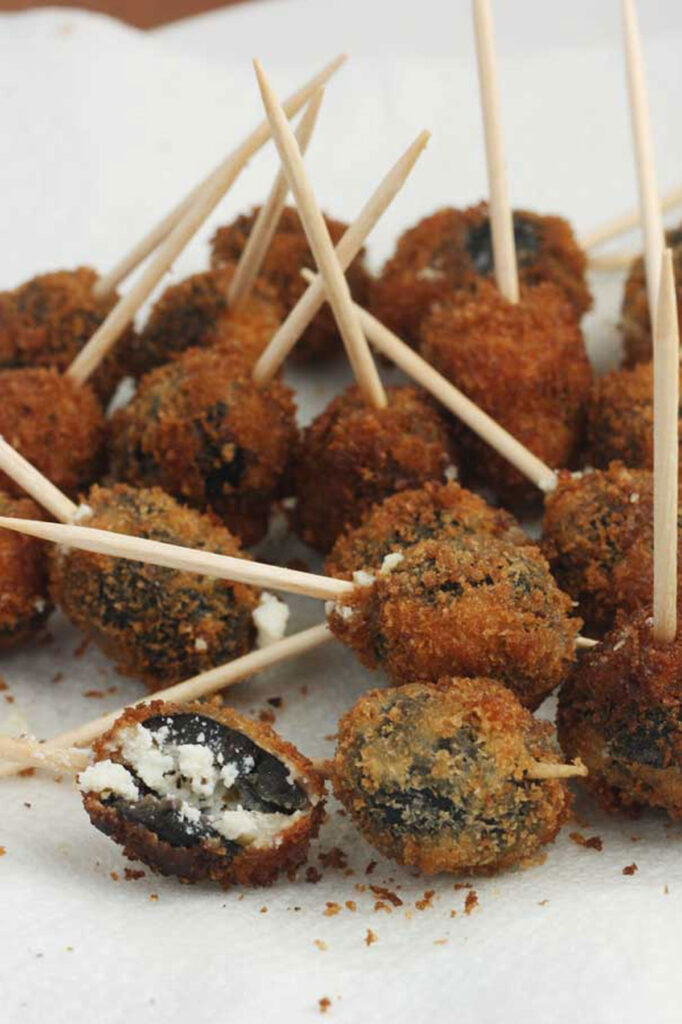 A plate of Greek fried olives with a cocktail stick in them on baking paper on a white plate