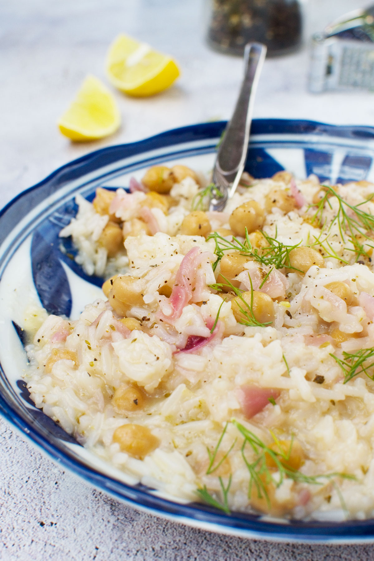 A plate of lemony Mediterranean rice with chickpeas in a blue bowl and with a spoon in it