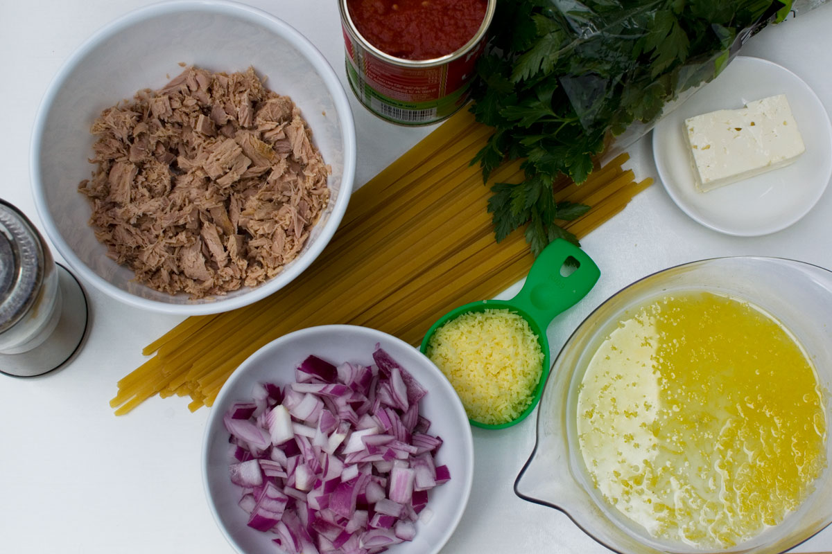 A photo showing the main ingredients for lemony tuna spaghetti: tuna, onion, tomatoes, spaghetti, lemon, parmesan, feta, pepper