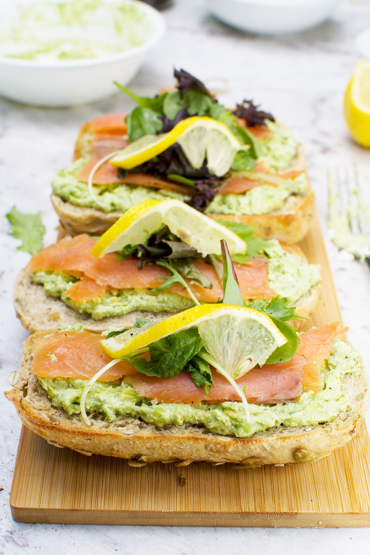 4 smoked salmon bruschettas with smashed avocado and feta on a wooden chopping board