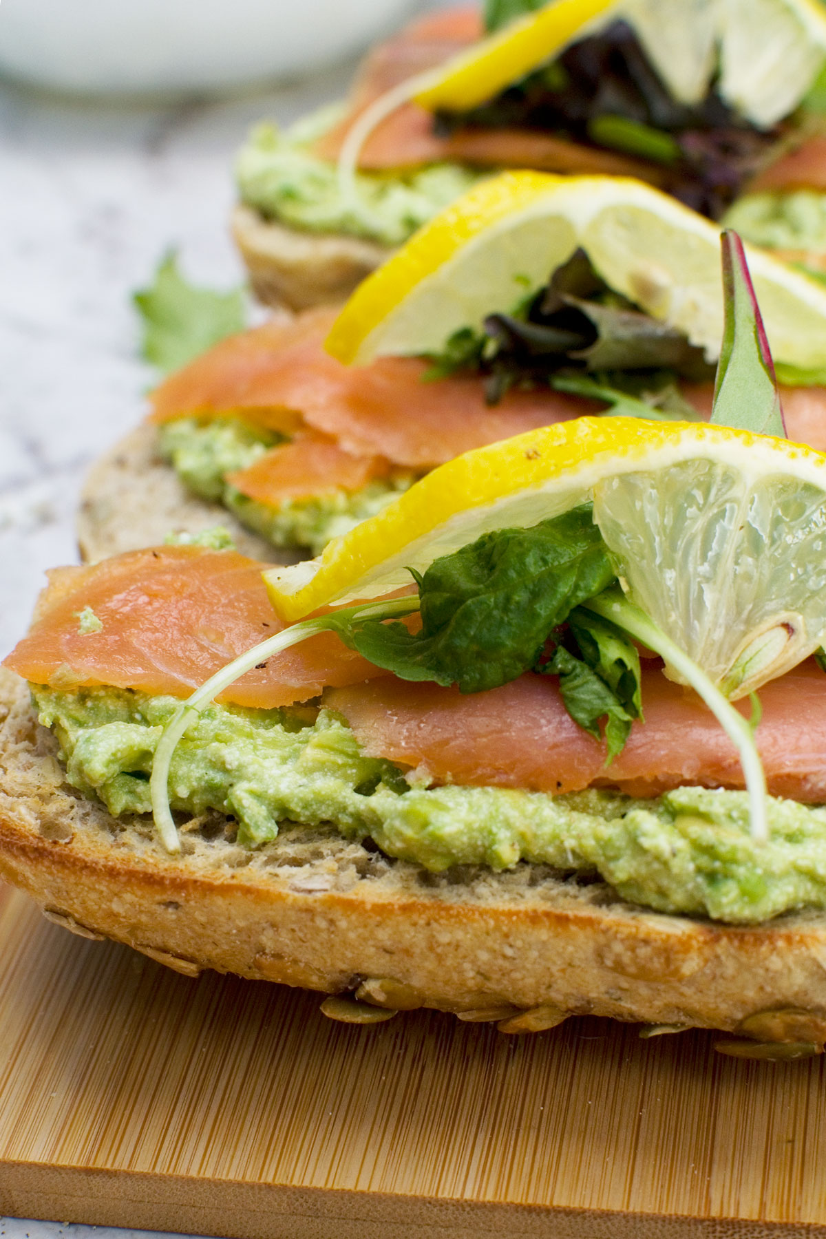 A close up of a wooden board of smoked salmon bruschetta with smashed avocado and feta