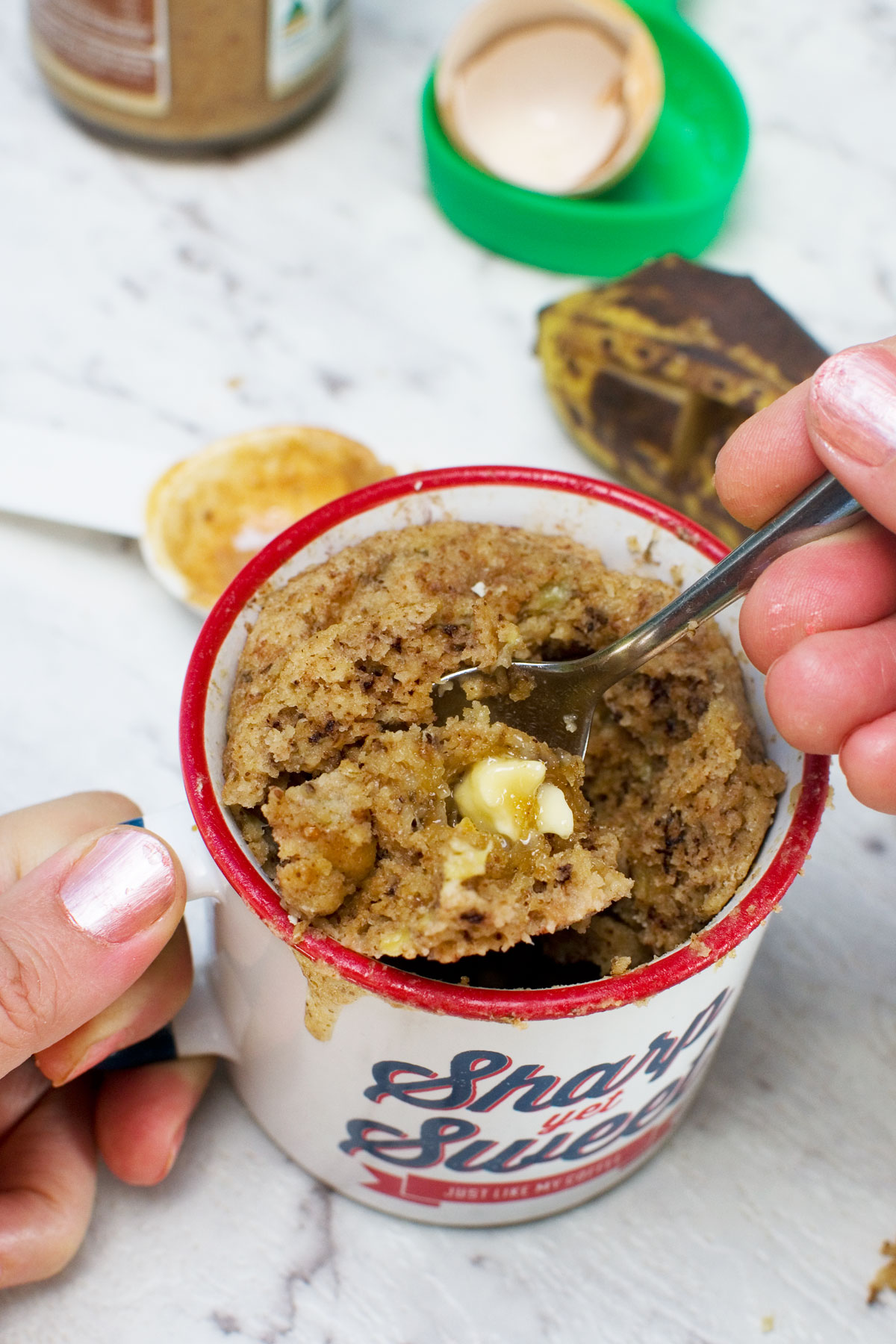 someone eating a gluten free banana mug cake with a spoon - various ingredients are scattered around