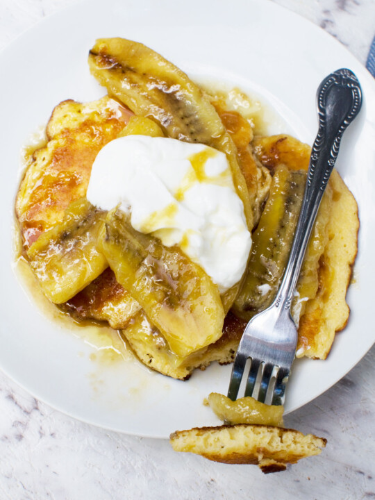 A plate of caramelised banana pancakes from above on a marble background - there's also a fork with a mouthful of pancake on it
