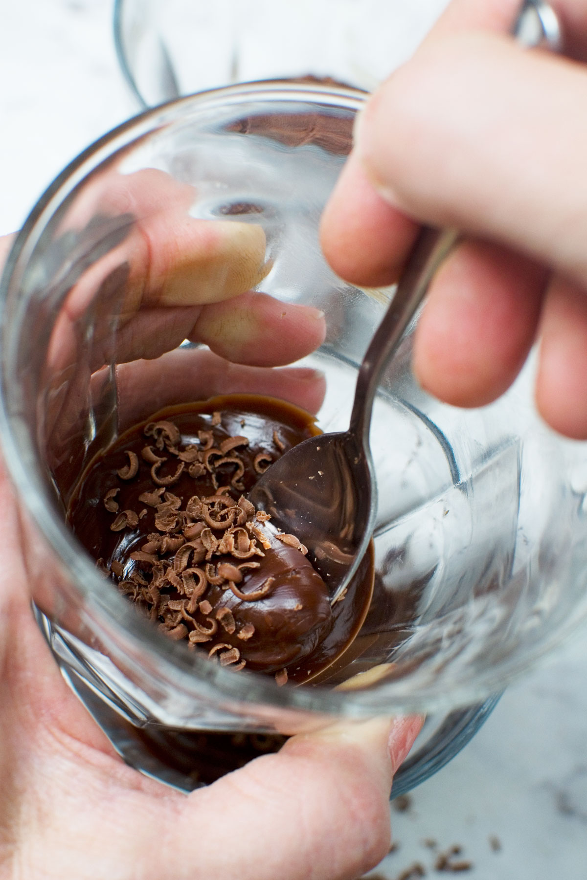 A closeup of someone holding a small glass and eating a chocolate pot with a spoon