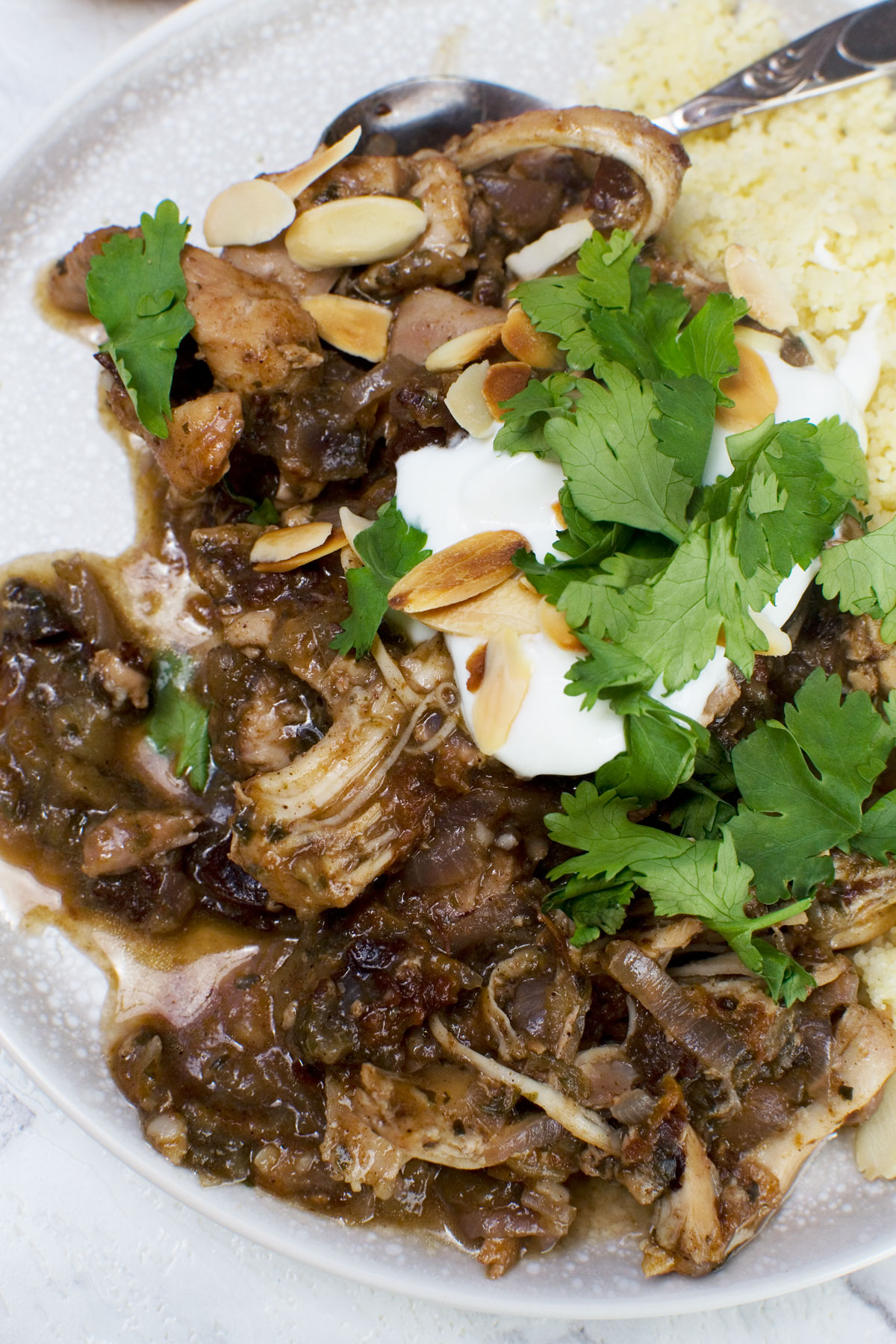 An overhead shot of a plate of Moroccan chicken stew with yogurt and fresh coriander on it and a spoon on a white plate