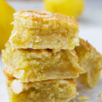 A stack of three lemon bakewell slices with lemons in the background