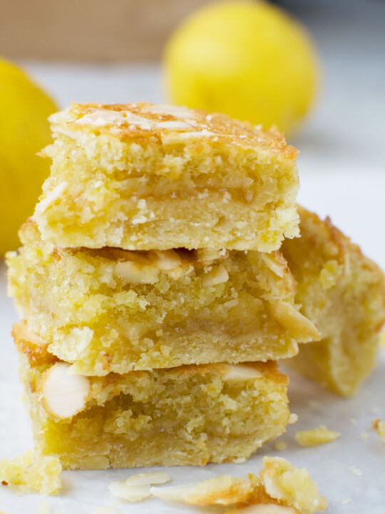 A stack of three lemon bakewell slices with lemons in the background