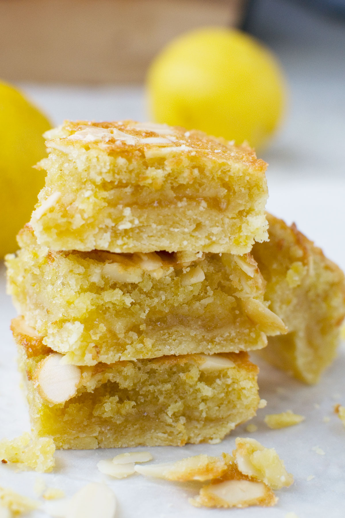 A stack of three lemon bakewell slices with lemons in the background