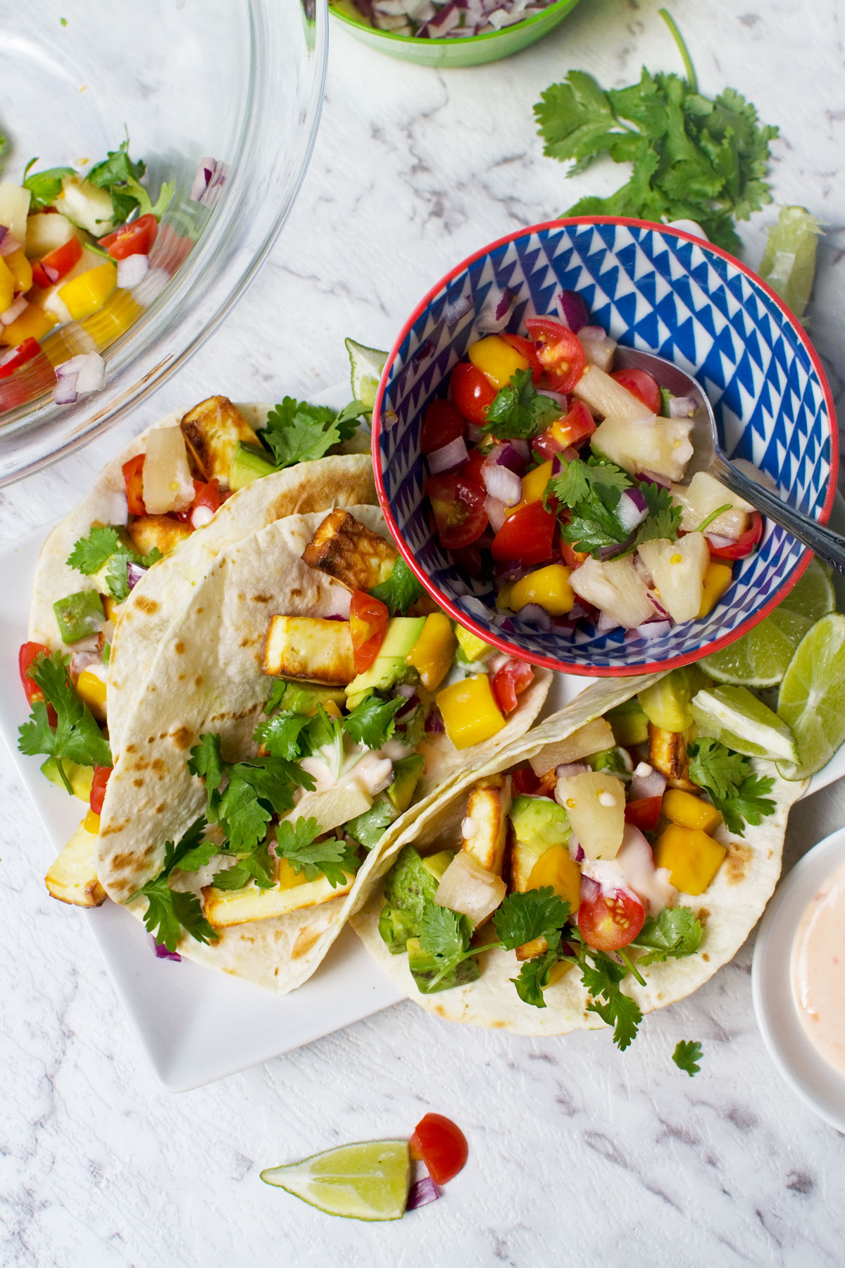 An overhead shot of 3 halloumi tacos with pineapple mango salsa on a white plate with a dish of the salsa