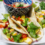 3 halloumi tacos with pineapple mango salsa on a white plate with a bowl of the salsa