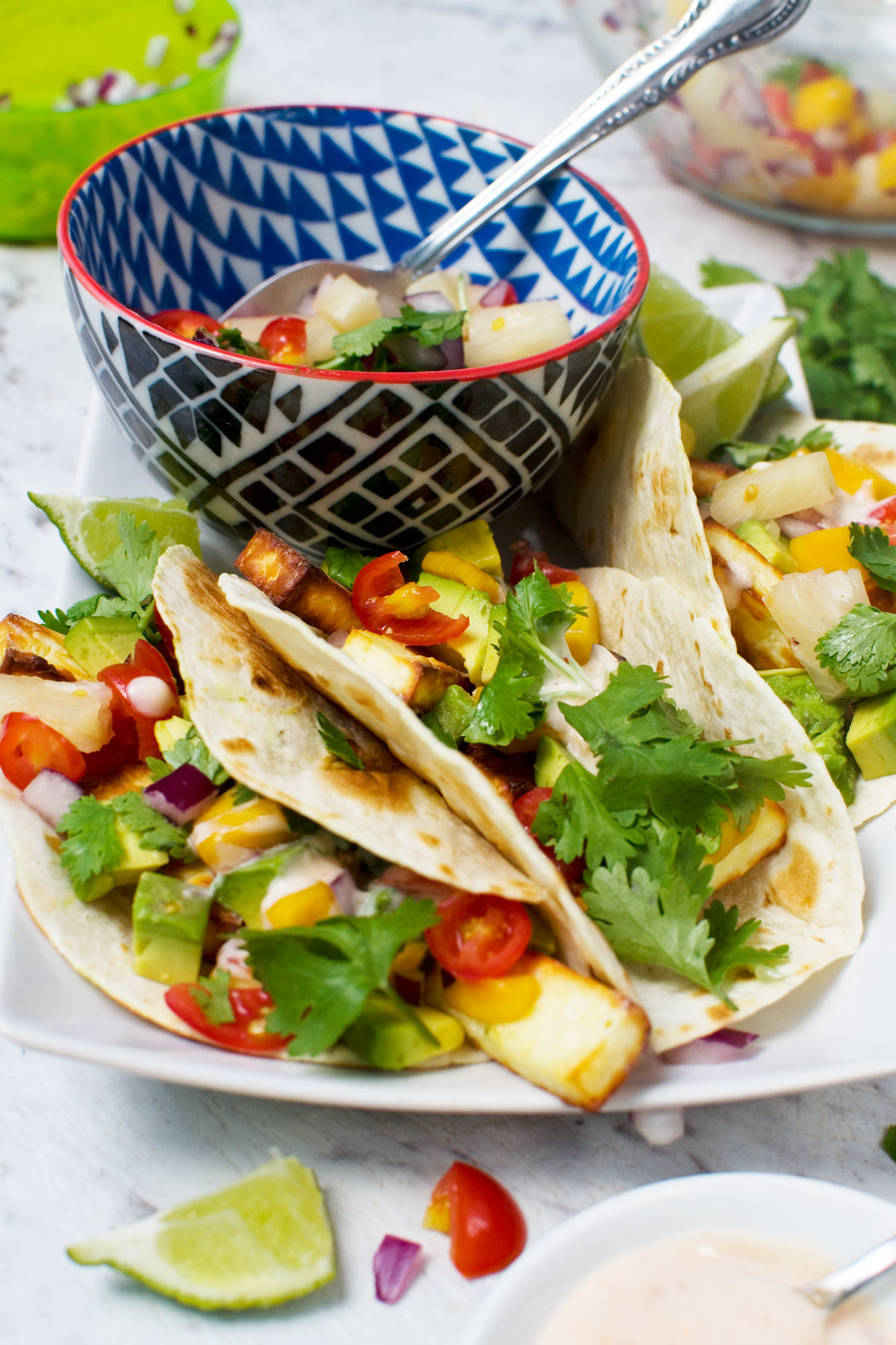 3 halloumi tacos with pineapple mango salsa on a white plate with a bowl of the salsa 