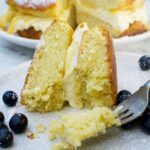Someone eating a slice of lemon mascarpone cake on a pale beige plate with blueberries with a fork