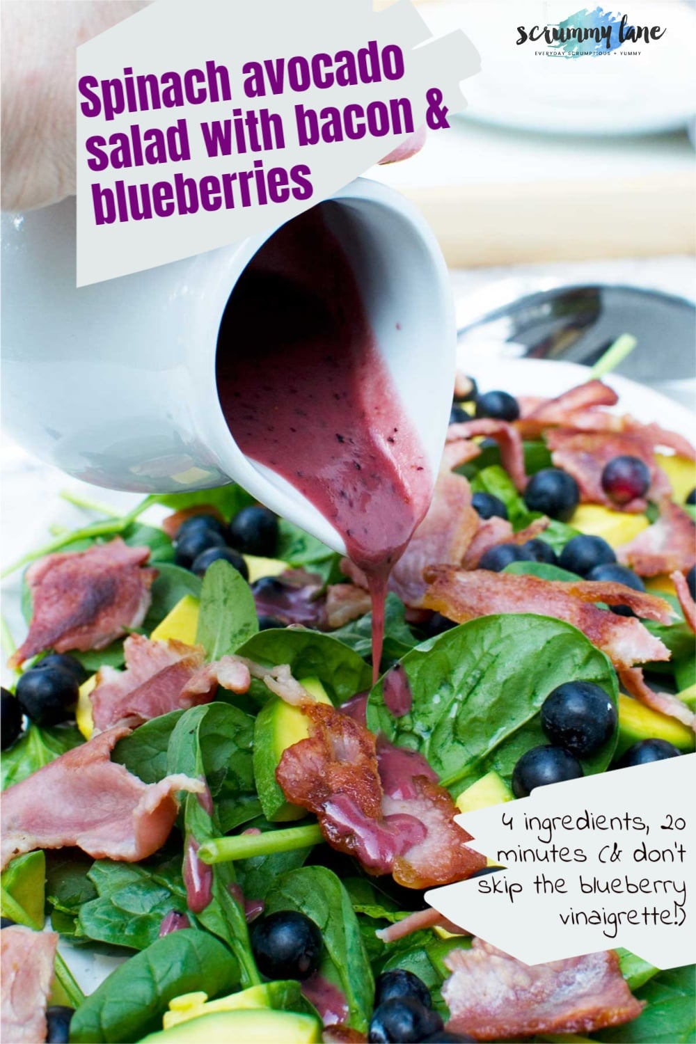 Someone pouring blueberry vinaigrette onto a spinach avocado salad with bacon and blueberries from a white jug and there's a title and subtitle on it