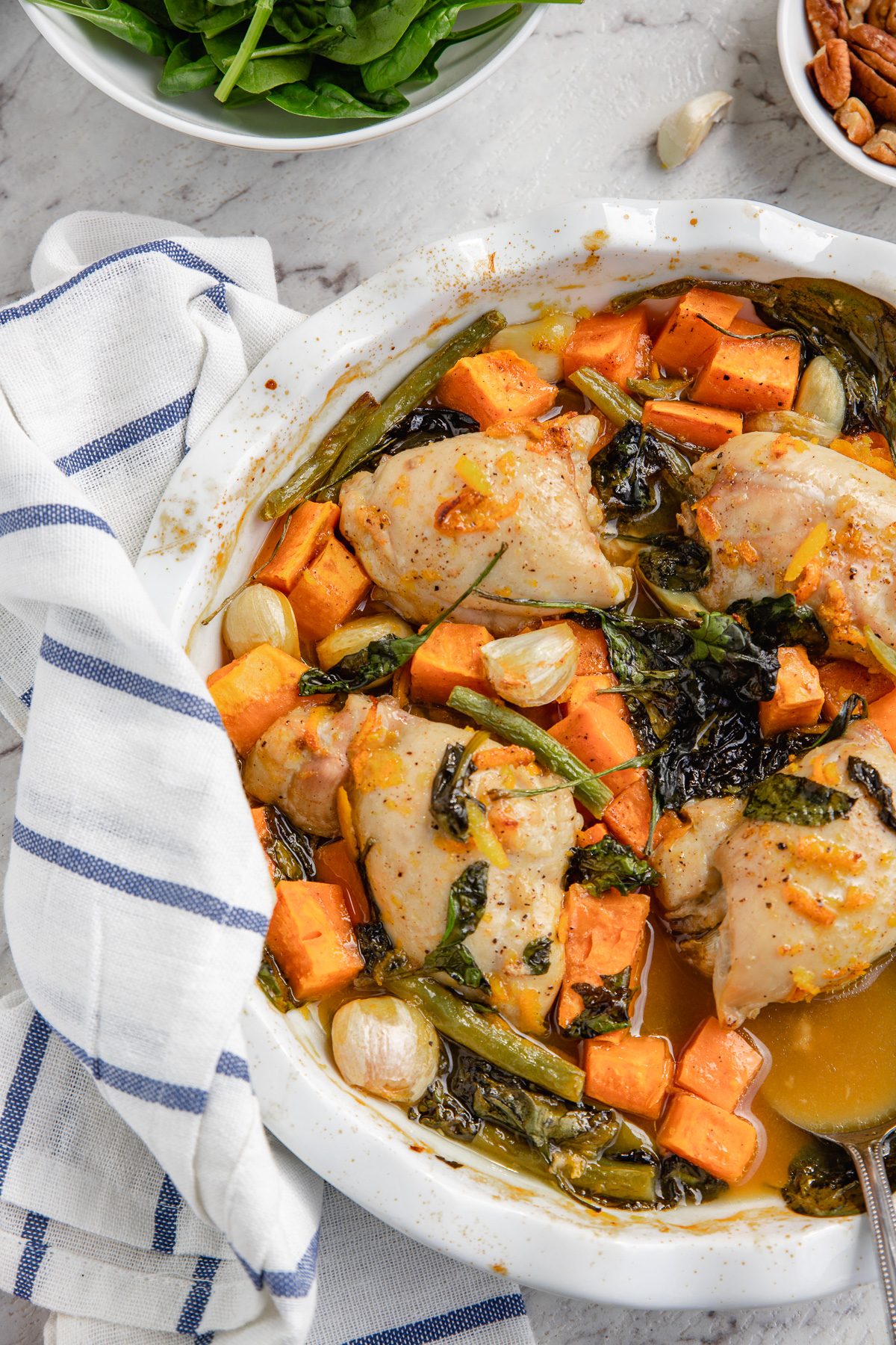 Half a dish of chicken and sweet potatoes with maple orange sauce from above with a blue striped tea towel