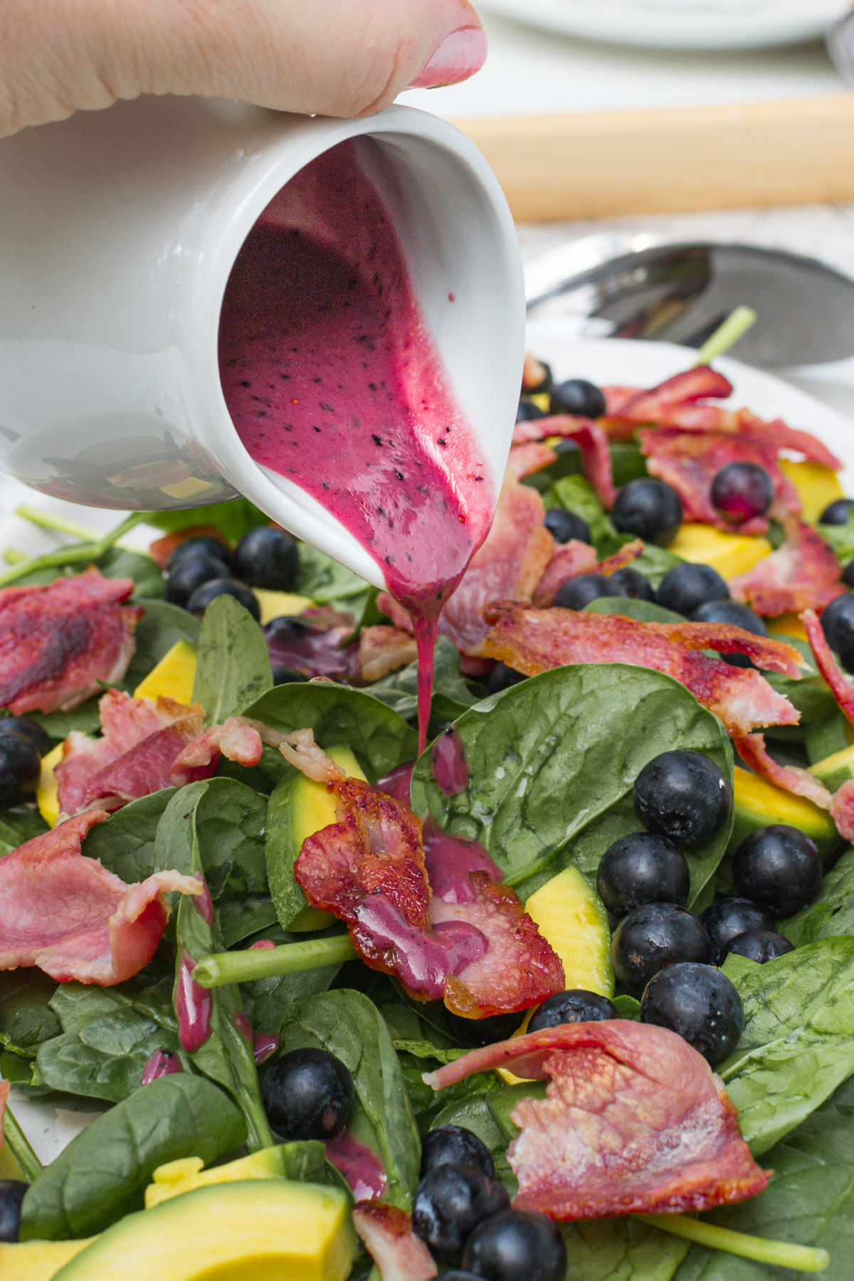 Closeup of someone pouring blueberry dressing onto a spinach avocado salad