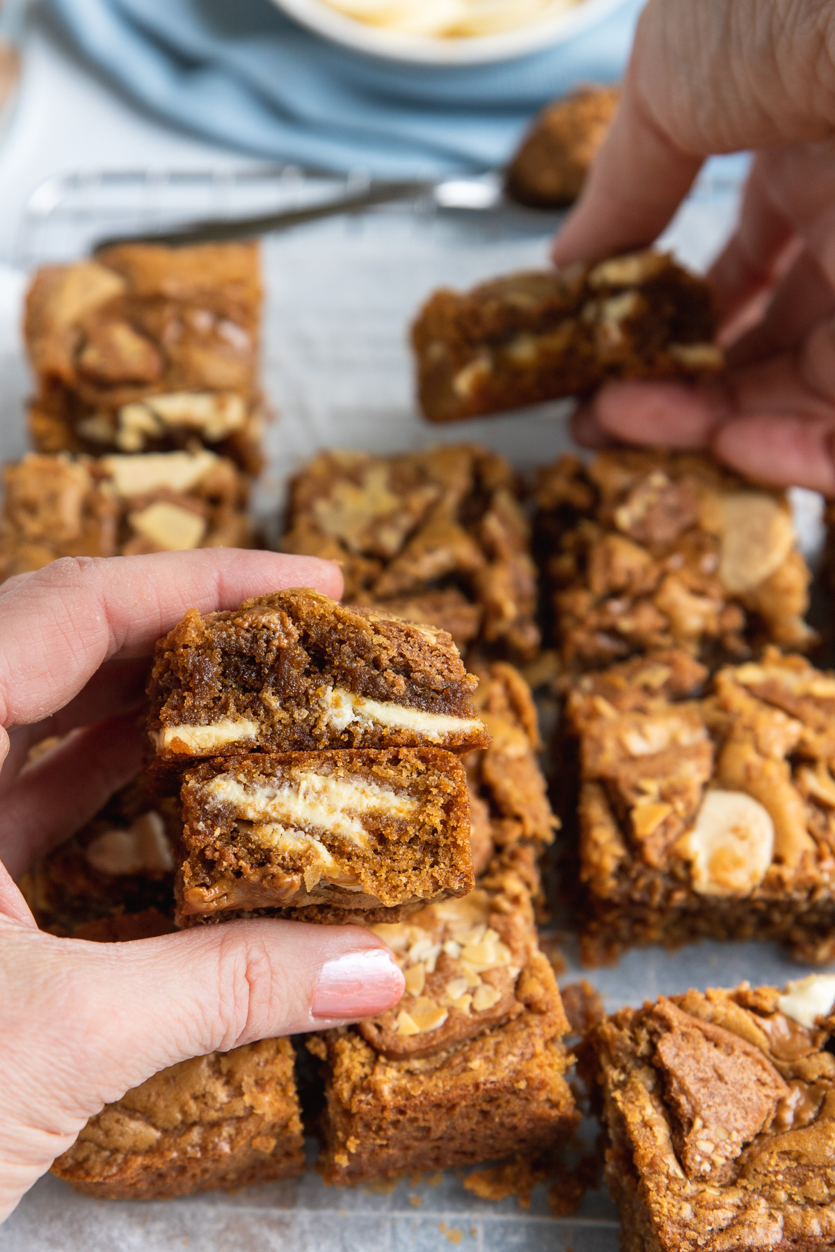 Someone holding a stack of two Biscoff blondies over the others in the pan with someone else taking a blondie in the background