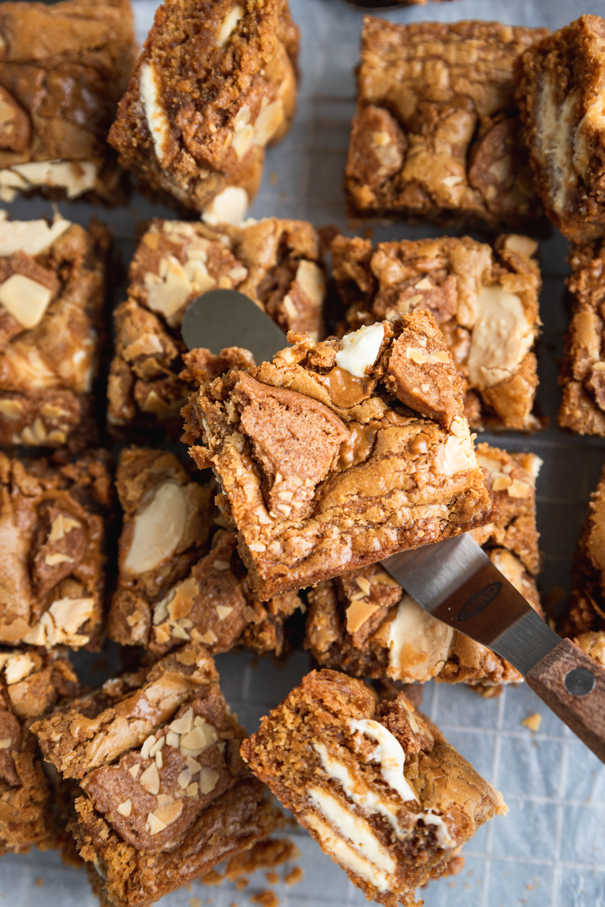 Biscoff blondies on baking paper from above, with someone holding up one above the others on a flat knife
