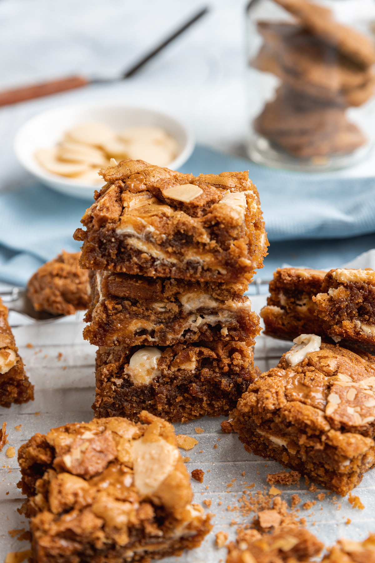 A stack of 3 Biscoff blondies on a wire cooking rack with ingredients in the background and other blondies all around