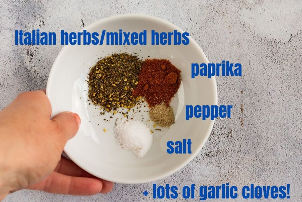 A person holding a small dish of herbs and spices for Mediterranean roast vegetables - so mixed herbs, paprika, pepper, salt and garlic cloves