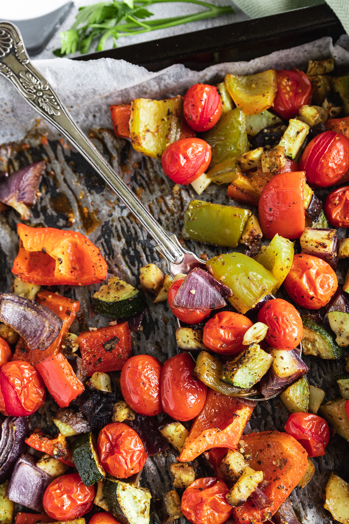 Closeup of baking tray of Mediterranean roast vegetables with a spoon in it