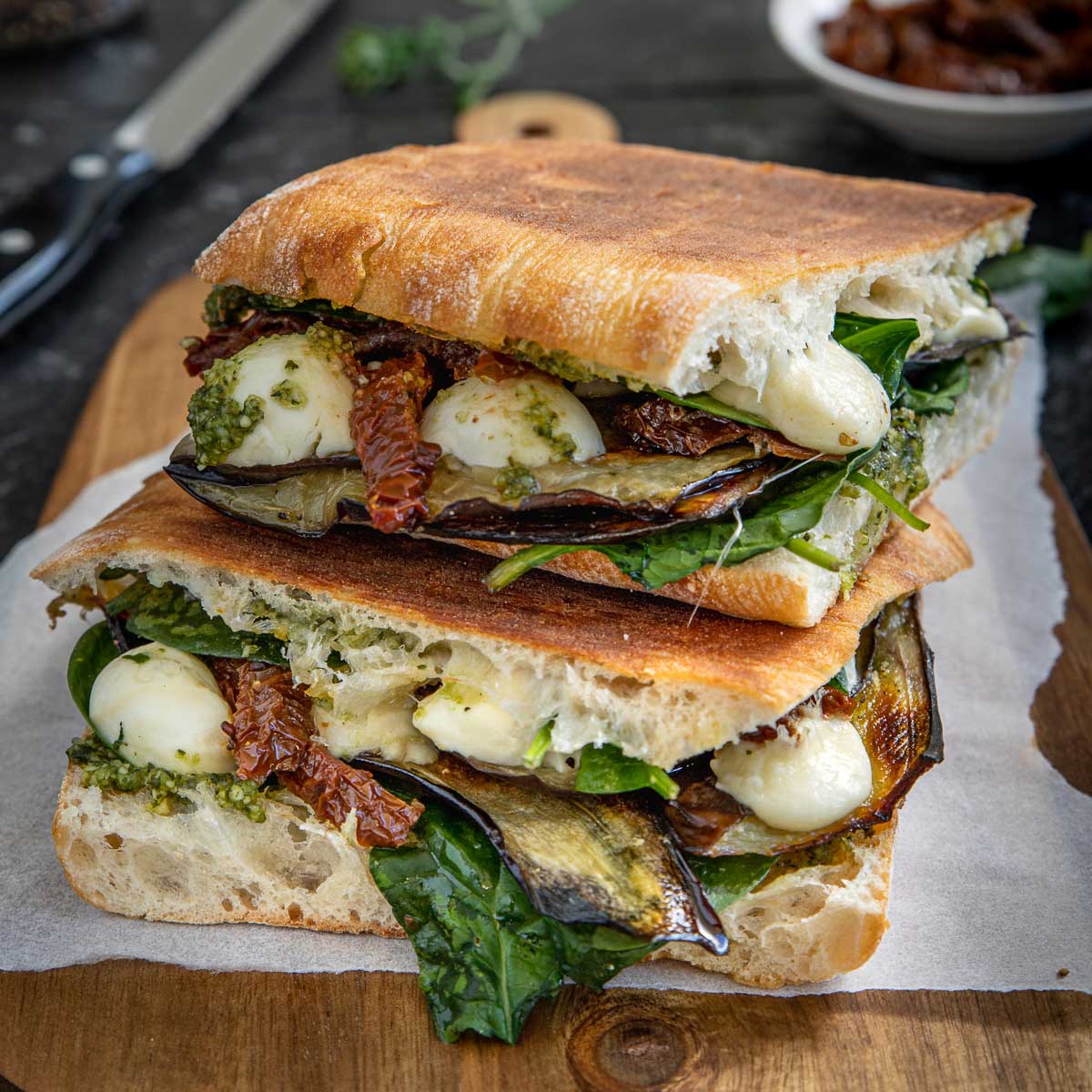 2 toasted veggie sandwiches stacked on top of each other on a wooden board