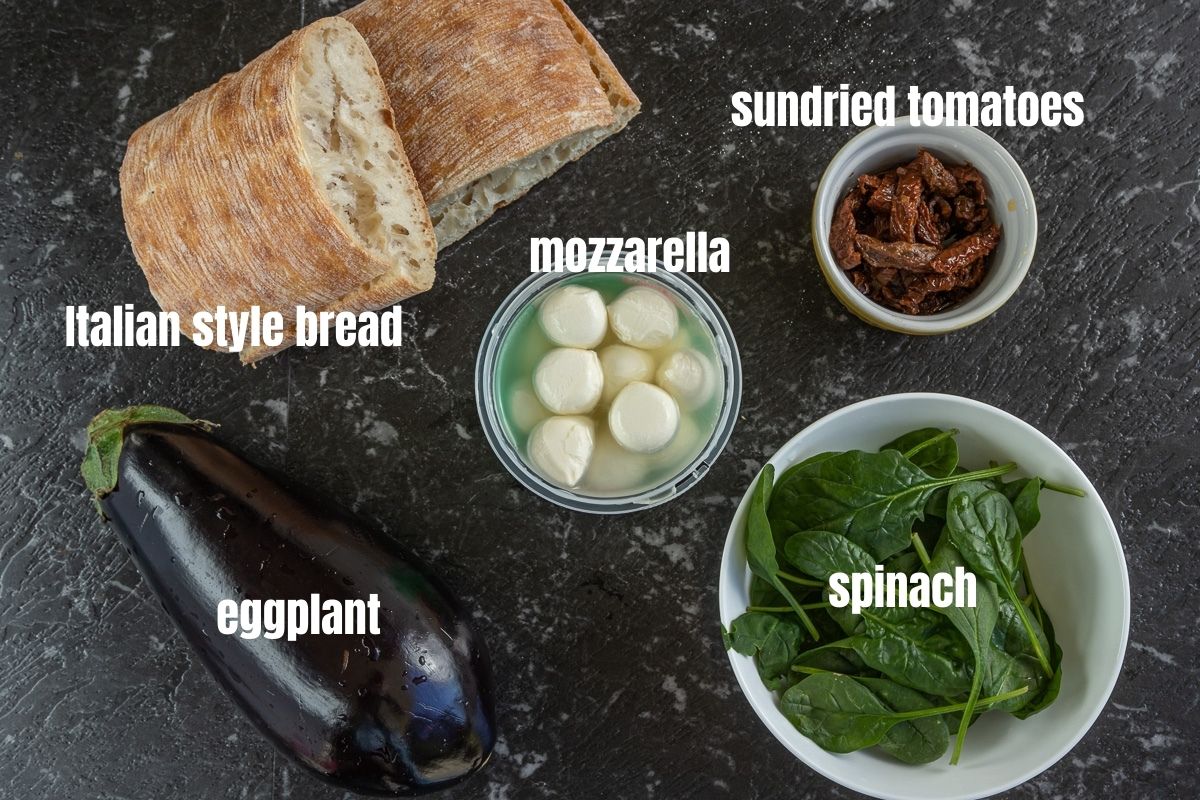 Pictures of the ingredients needed to make an Italian veggie sandwich: eggplant, Italian style bread, mozzarella balls, sundried tomatoes, spinach