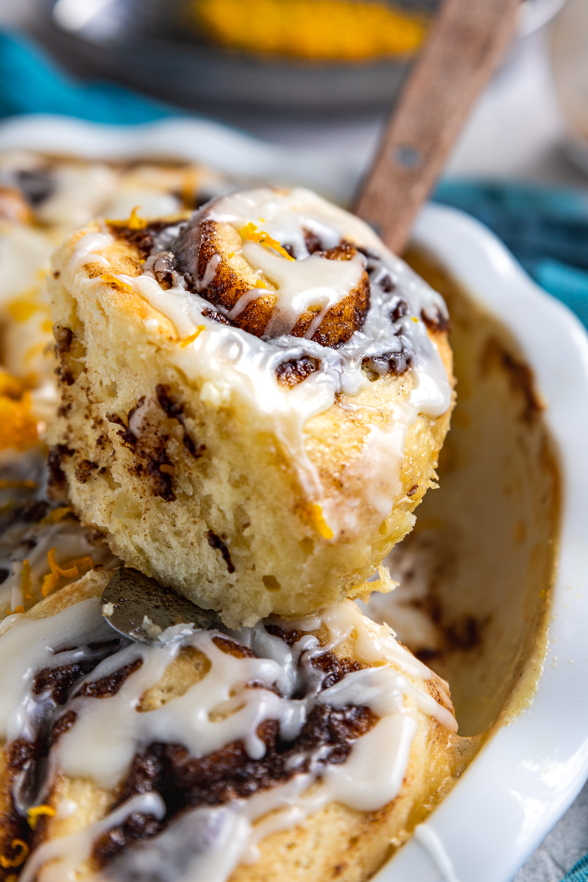 Closeup of someone taking a cinnamon scroll out of the pan with a wooden handled palette knife