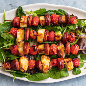 A platter of halloumi kebabs with chorizo and tomatoes from above on a blue-grey background