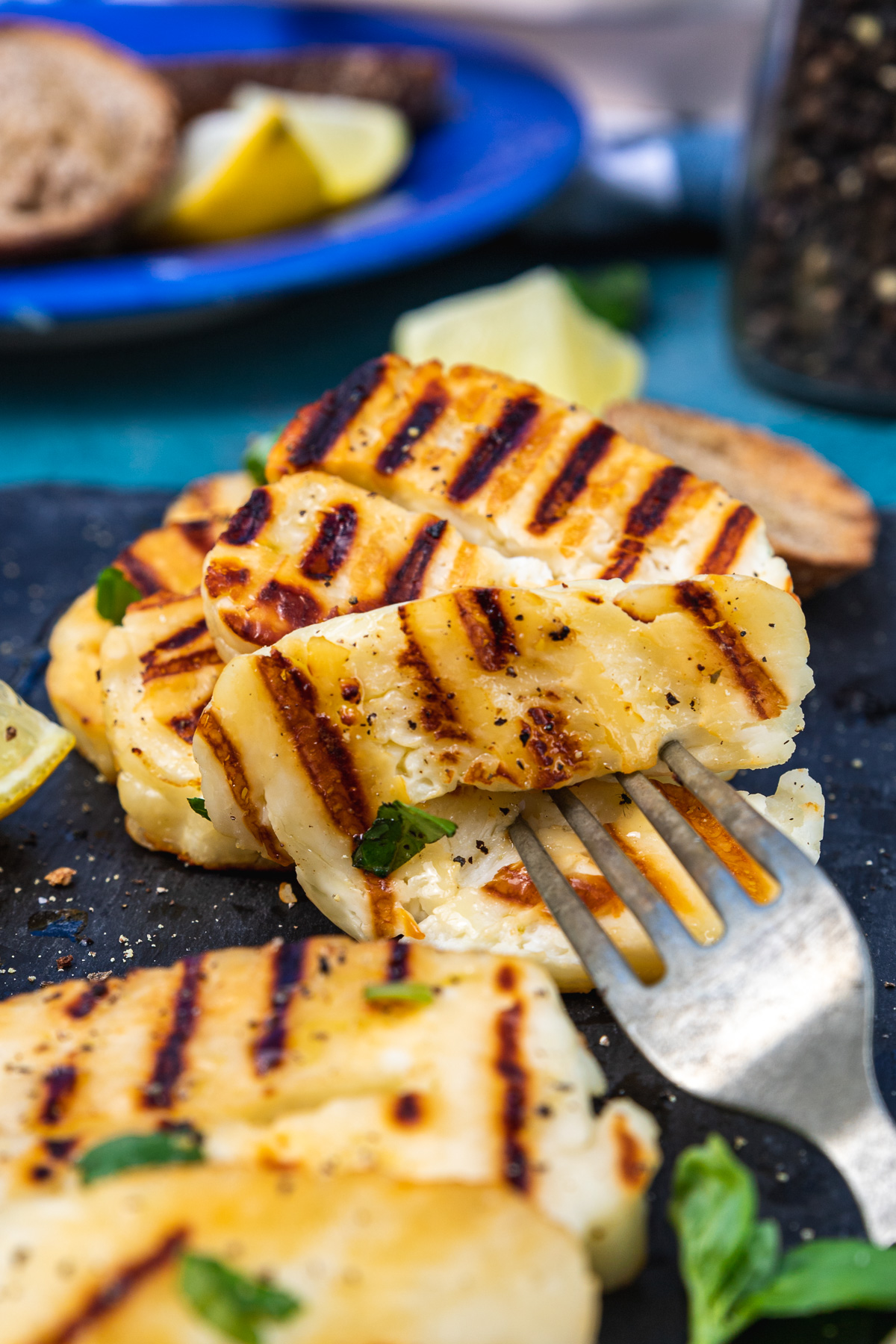 Closeup of someone grabbing a piece of grilled halloumi with a fork from a black platter with more in the background