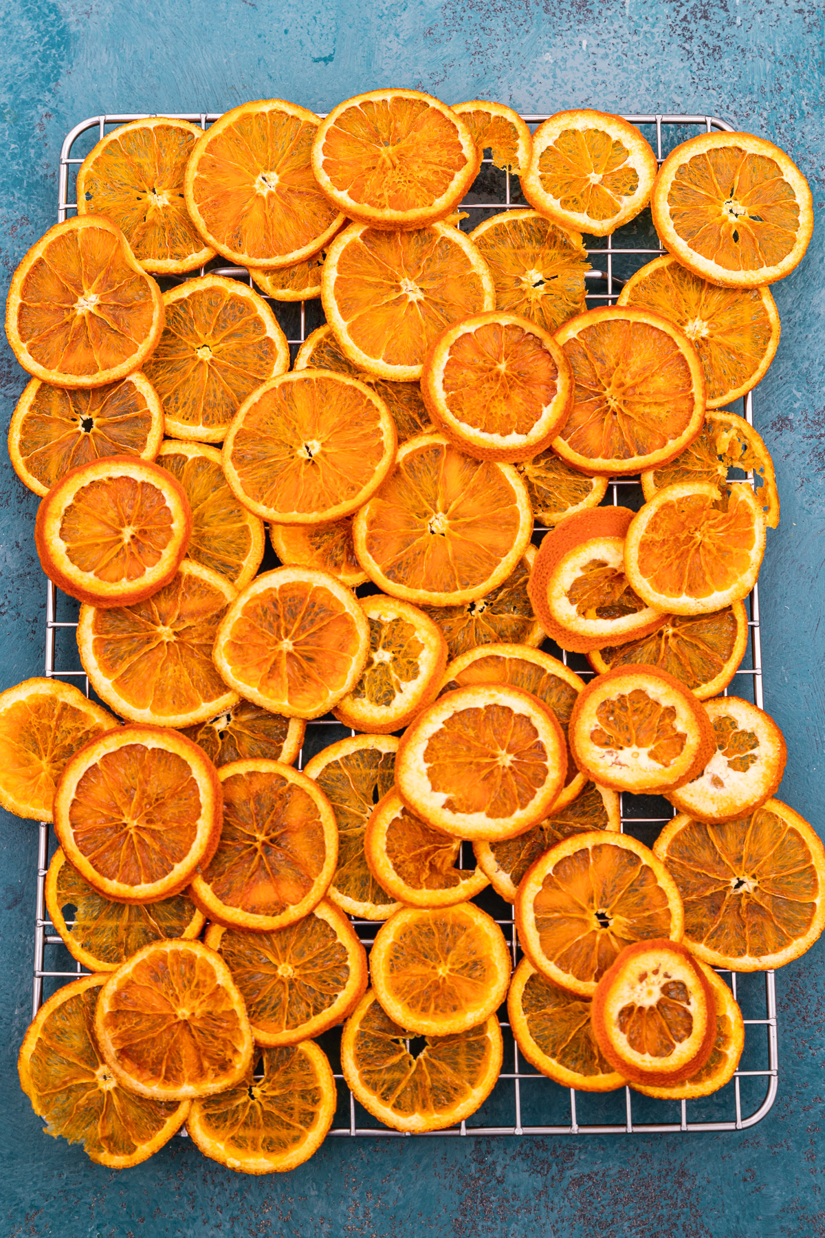 Dried orange slices from above piled onto a wire rack and on a blue background