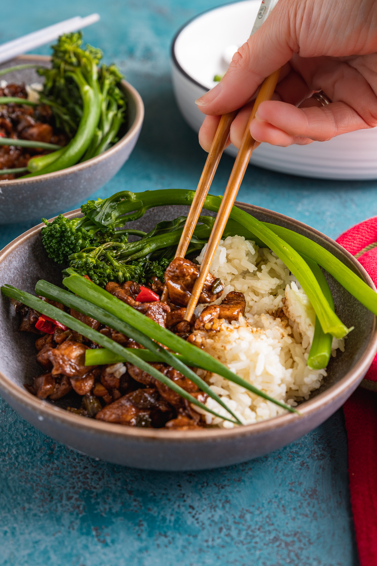 Someone eating Shanghai chicken with rice with chopsticks from a blue grey bowl on a blue background