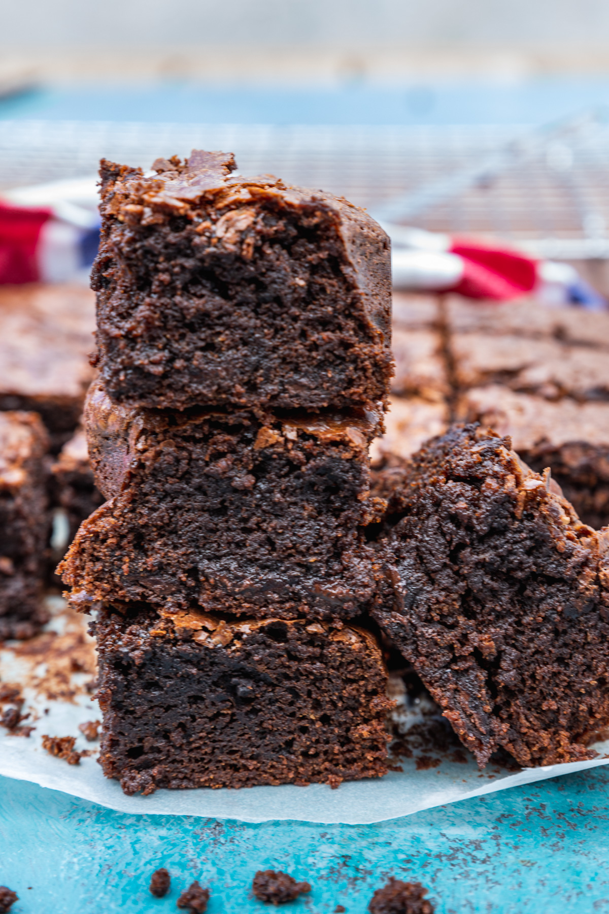 A stack of 3 gluten-free brownies on a blue background and with the rest of the pan in the background