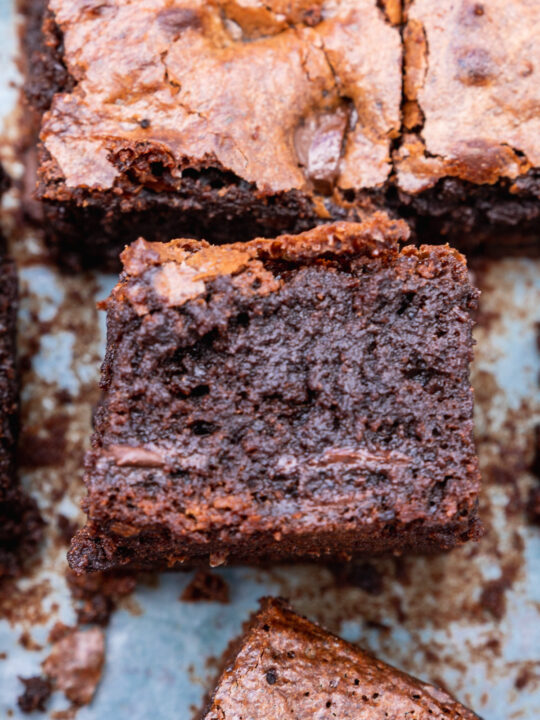 A gluten-free chocolate brownie on its side on a piece of baking paper with others from above