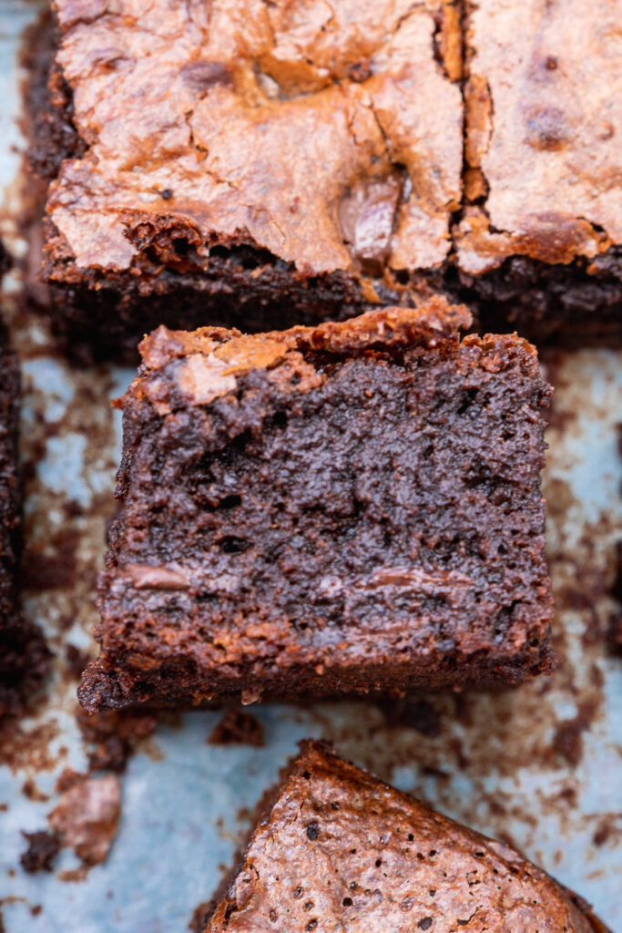 A gluten-free chocolate brownie on its side on a piece of baking paper with others from above