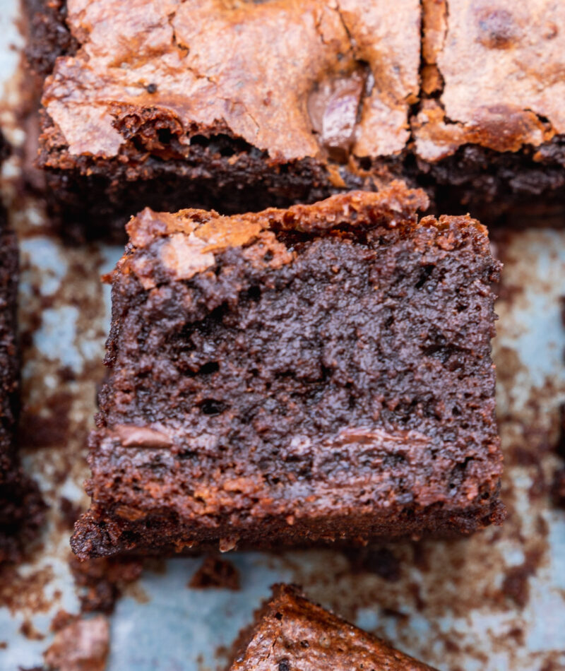 A gluten-free chocolate brownie on its side on a piece of baking paper with others from above