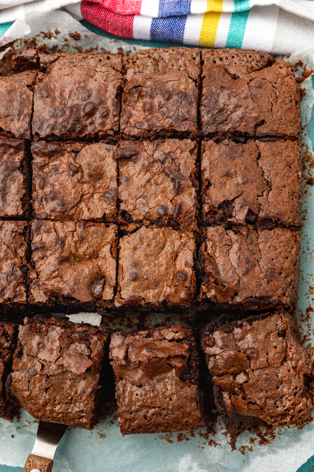 A pan of sliced brownies from above and with a multi-coloured striped tea towel above it 