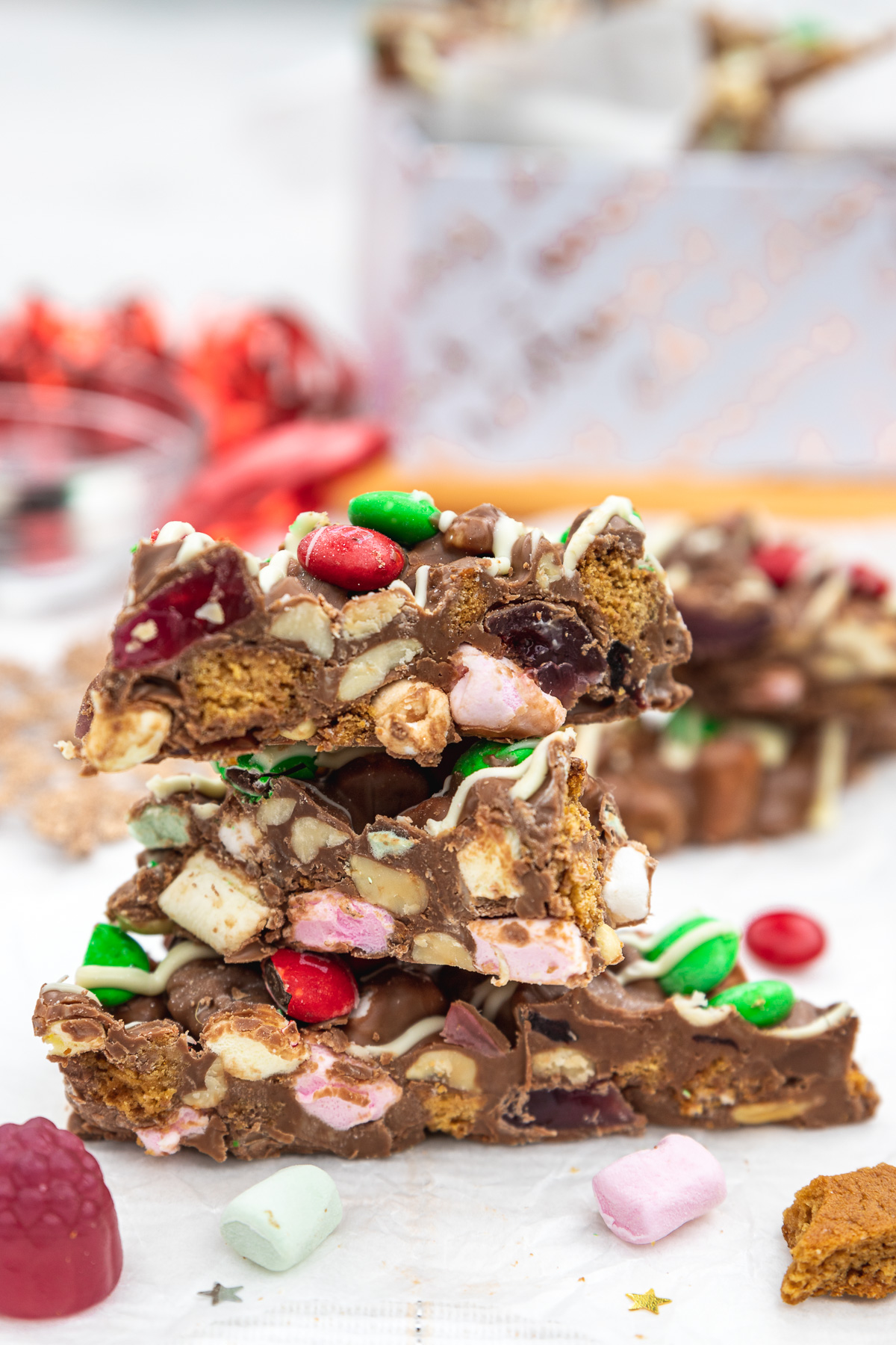 A small stack of Christmas rocky road on a white background with ingredients and decorations around it