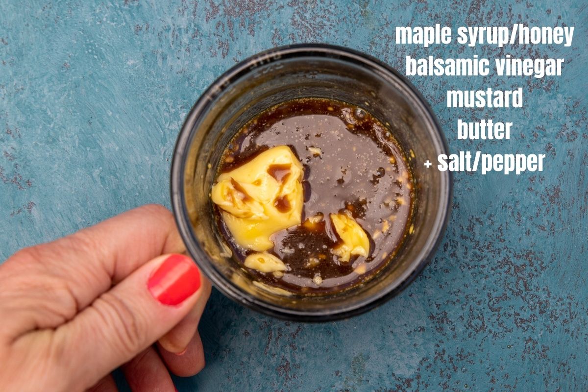 Someone holding Ingredients for honey mustard balsamic dressing for brussels sprouts and carrots in a glass cup on a blue background