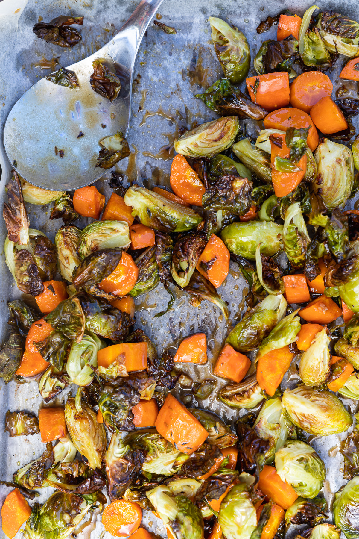 Roasted brussels sprouts and carrots on a baking tray from above with a serving spoon