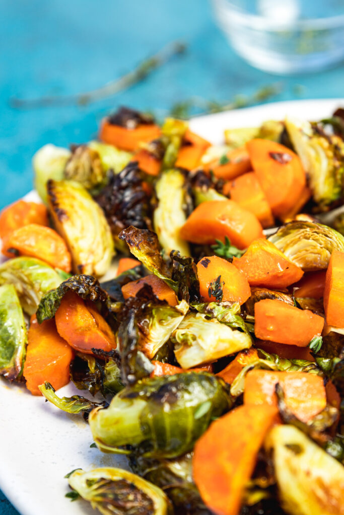 Close-up of brussels sprouts and carrots on a white plate with blue in the background
