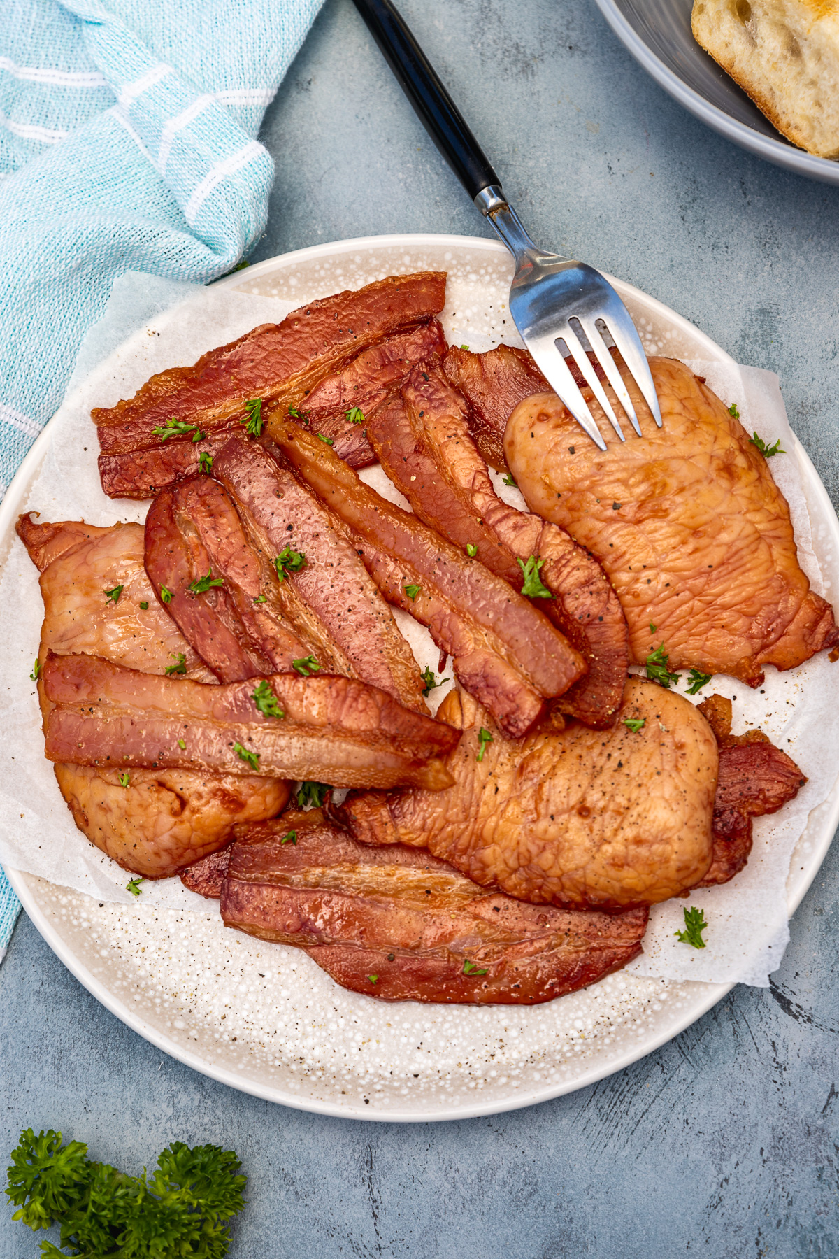 A plate of air fried bacon on a beige plate and blue background from above with a fork in it and with a blue tea towel