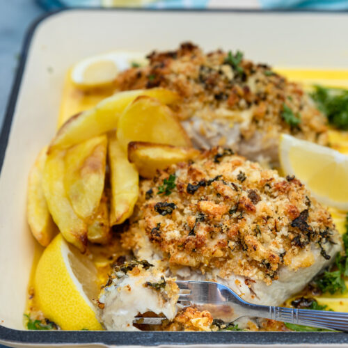 close-up of baked cod with panko topping in a cast iron pan and with a blue tea towel in the background