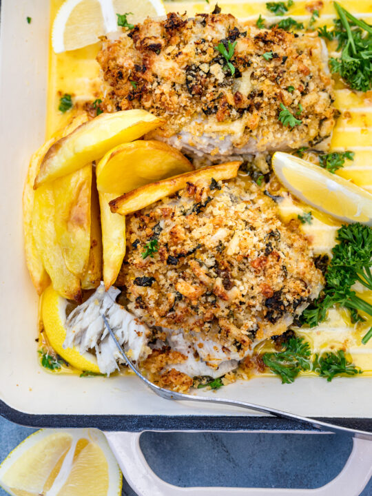 Baked cod with panko or posh fish and chips in a white cast iron pan from above on a blue background