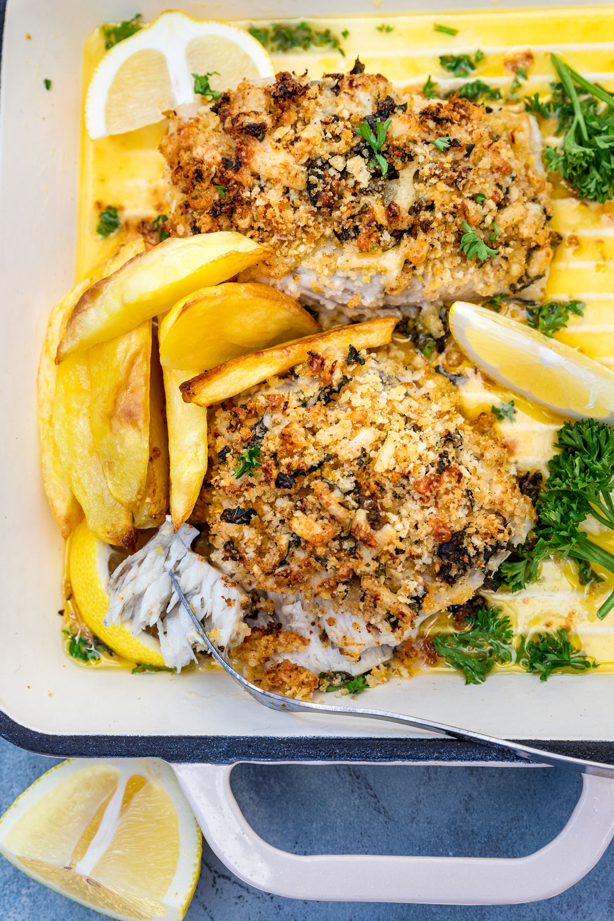 Baked cod with panko or posh fish and chips in a white cast iron pan from above on a blue background