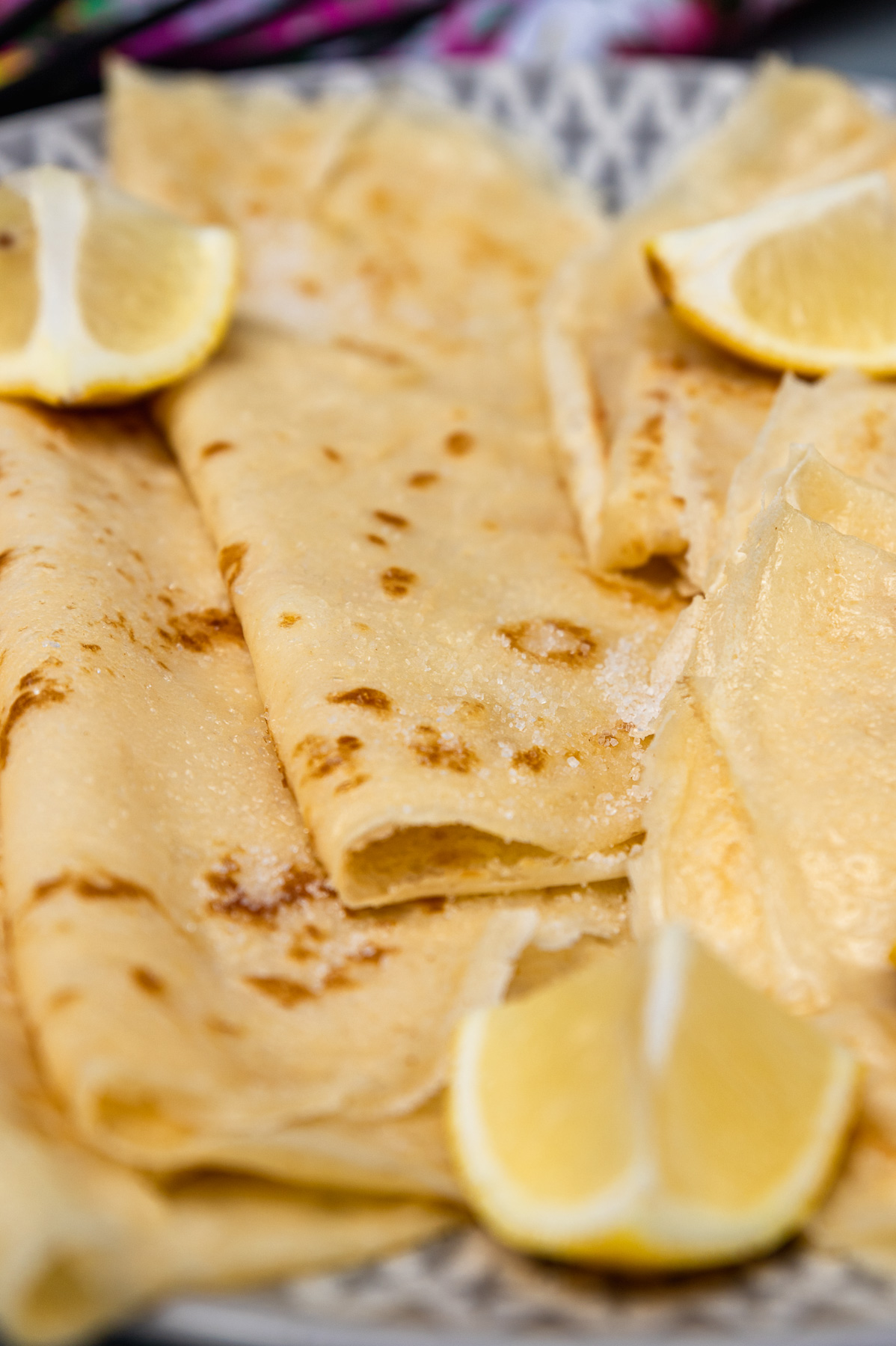 Closeup of thin English pancakes on a grey and white plate with sugar and lemon on top