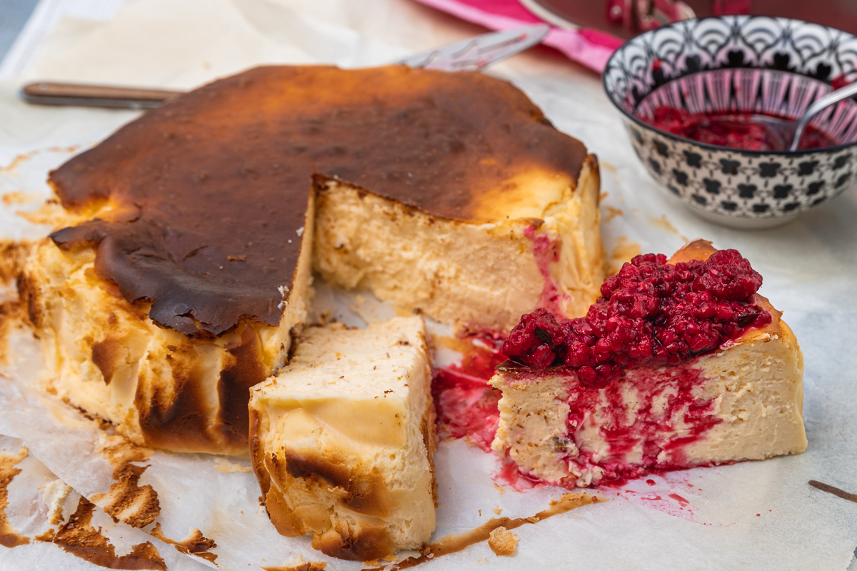 San Sebastian cheesecake with 2 pieces cut out of it and one with raspberries piled on it