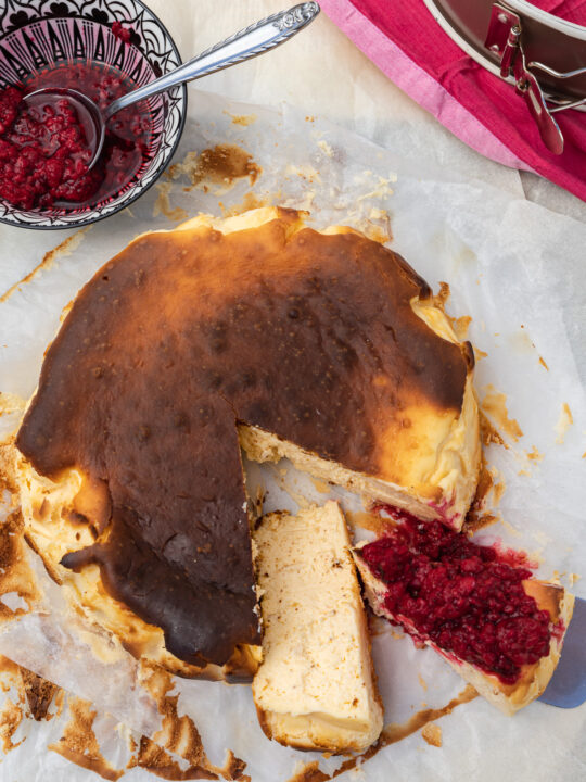 A San Sebastian cheesecake from above with pieces cut out and raspberries on the top of one piece