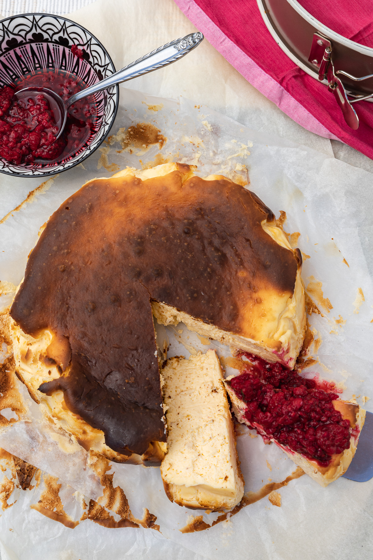 A San Sebastian cheesecake from above with pieces cut out and raspberries on the top of one piece