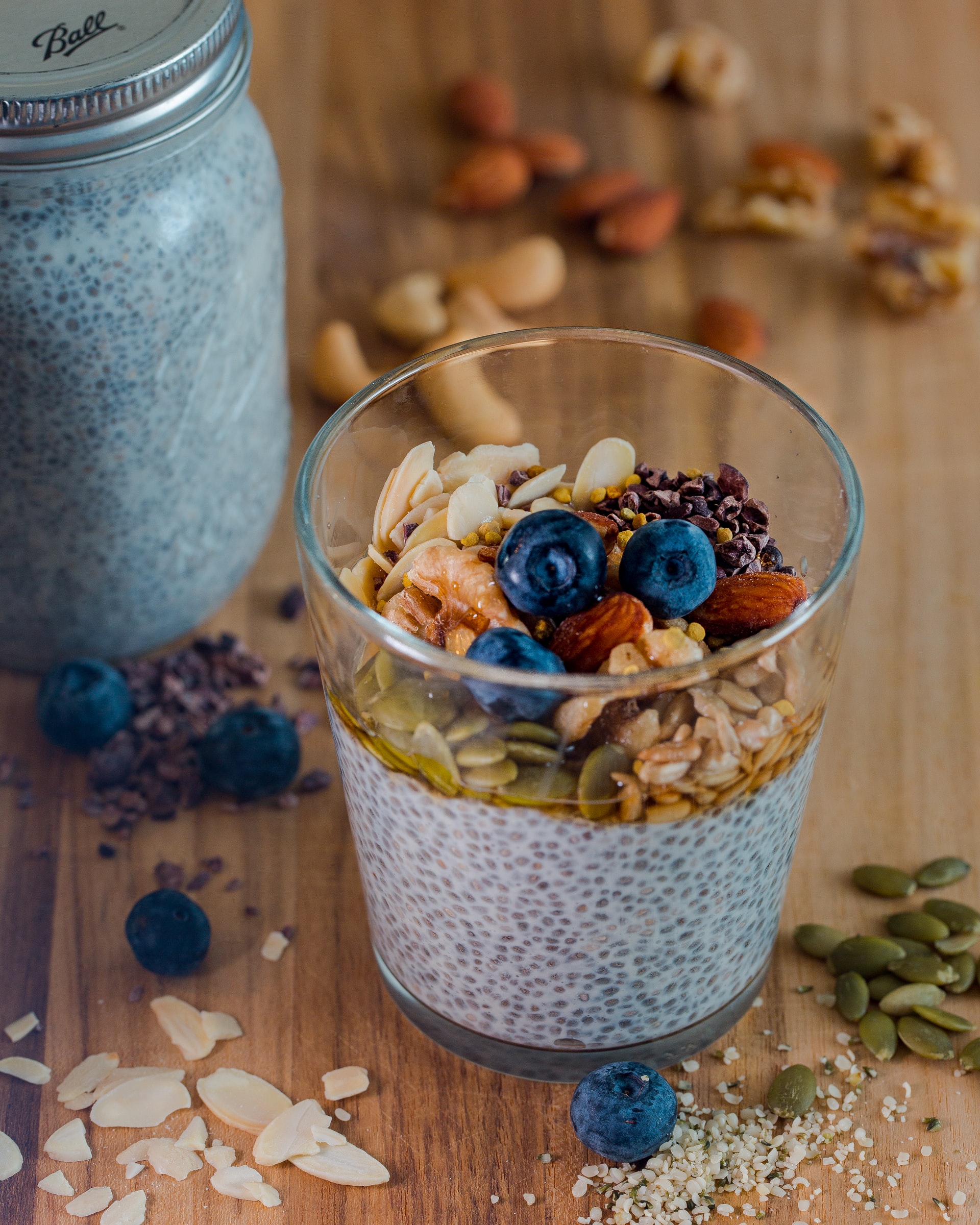 A glass of chia pudding with granola and berries on top and more granola scattered around