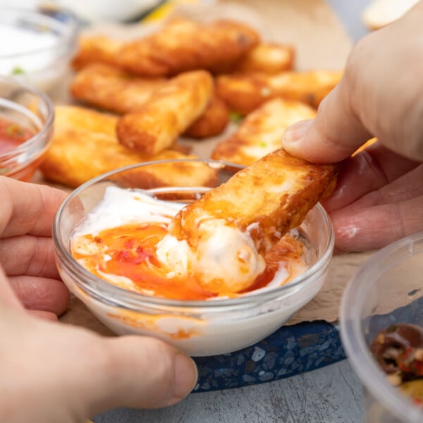 Someone dipping a crispy halloumi fry into a dip with a stack of fries in the background